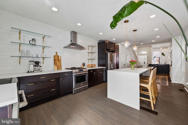 kitchen featuring a breakfast bar, appliances with stainless steel finishes, light countertops, wall chimney range hood, and a kitchen island