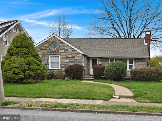 ranch-style home with a chimney, a shingled roof, stone siding, and a front lawn