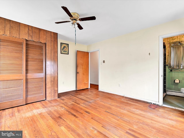 unfurnished bedroom with a closet, baseboards, a ceiling fan, hardwood / wood-style flooring, and ensuite bath