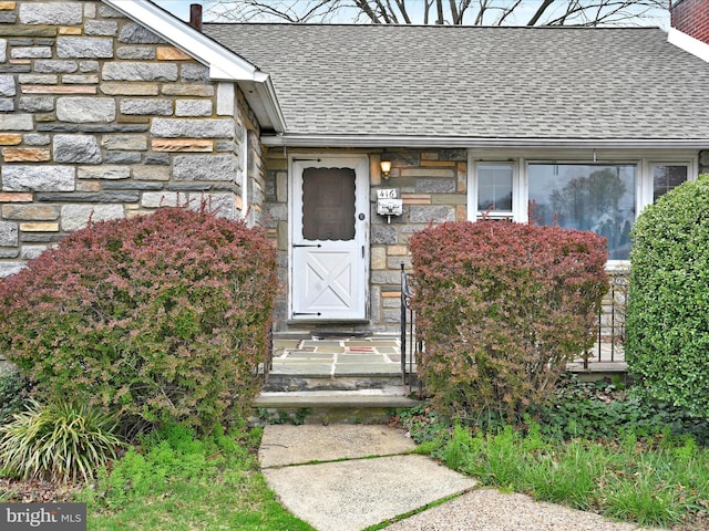 entrance to property with roof with shingles, a chimney, and stone siding