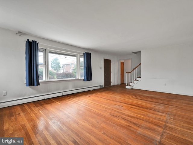 unfurnished living room featuring a baseboard radiator, wood finished floors, and stairs