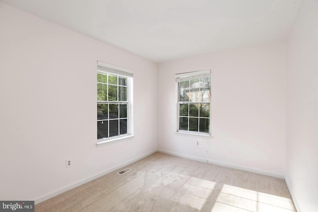 carpeted spare room featuring baseboards, visible vents, and a wealth of natural light