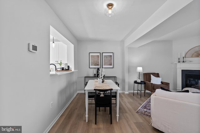 dining space featuring baseboards, a glass covered fireplace, and wood finished floors