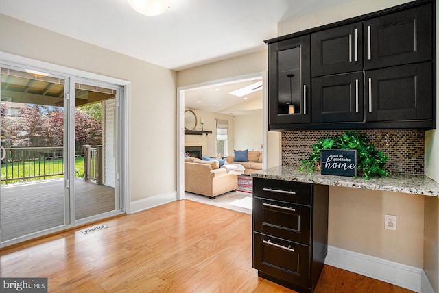 bar area with backsplash, a fireplace, light wood-style floors, and baseboards