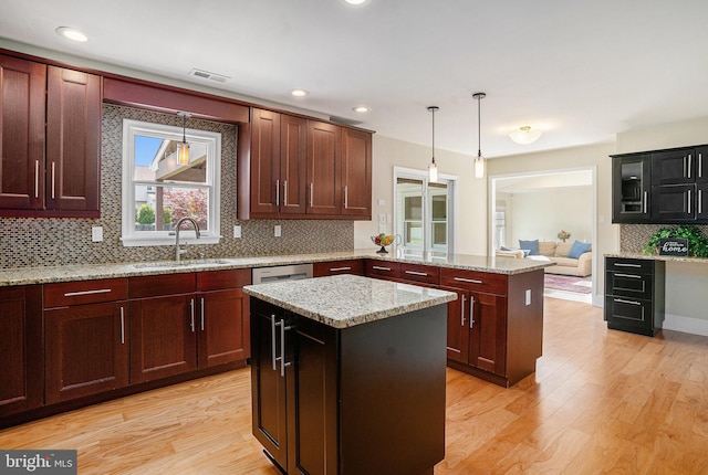 kitchen with a sink, a peninsula, light wood finished floors, decorative backsplash, and decorative light fixtures