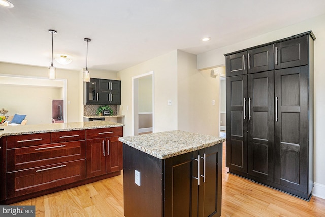 kitchen with light wood-style floors, pendant lighting, light stone countertops, a center island, and recessed lighting