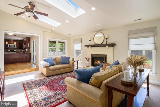 living area with lofted ceiling, a skylight, recessed lighting, a brick fireplace, and a ceiling fan