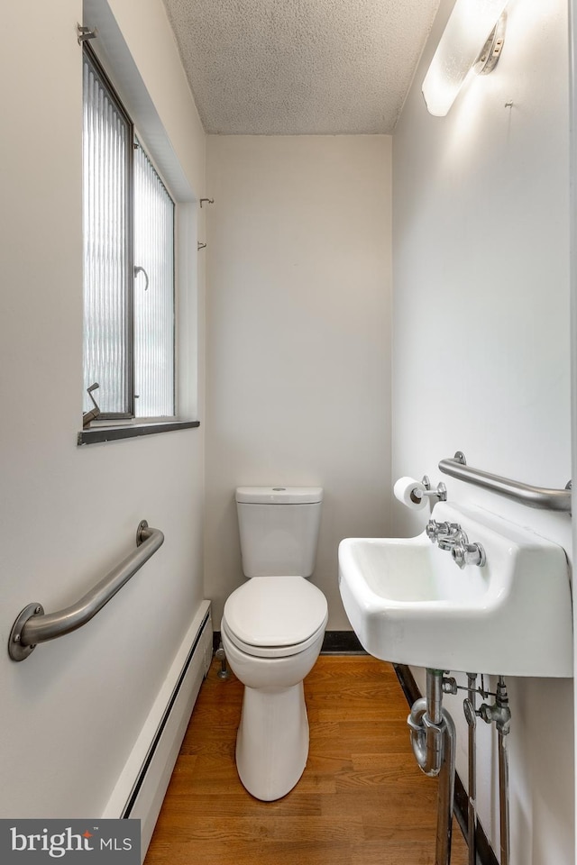 half bath featuring a baseboard heating unit, toilet, wood finished floors, and a textured ceiling