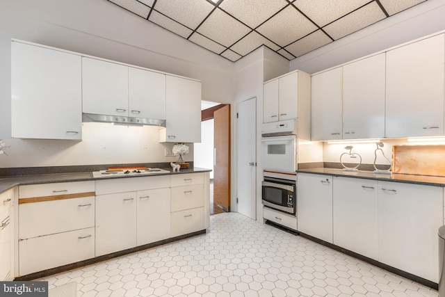 kitchen with white appliances, dark countertops, under cabinet range hood, and a drop ceiling