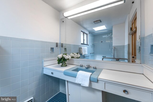 bathroom with a sink, visible vents, a wainscoted wall, tile walls, and tiled shower