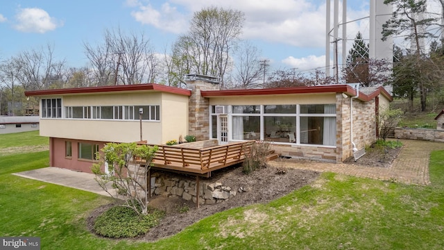 back of house featuring a wooden deck, a lawn, stone siding, a chimney, and stucco siding