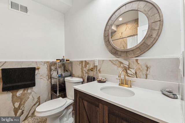 full bathroom featuring a wainscoted wall, visible vents, toilet, vanity, and tile walls