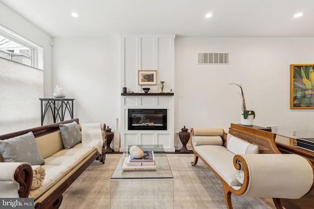living room featuring a glass covered fireplace, wood finished floors, visible vents, and recessed lighting
