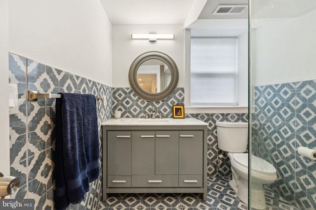 bathroom featuring wainscoting, vanity, tile walls, toilet, and visible vents