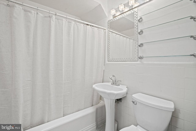 full bathroom with tile walls, toilet, a sink, and shower / bath combination with curtain