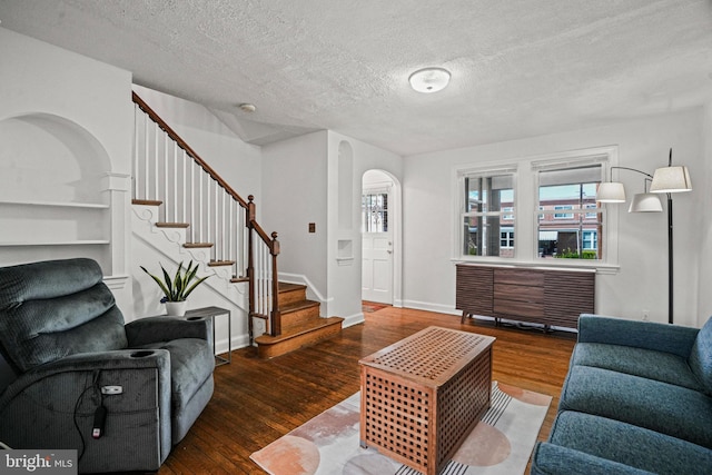 living room with a textured ceiling, wood finished floors, arched walkways, and stairs