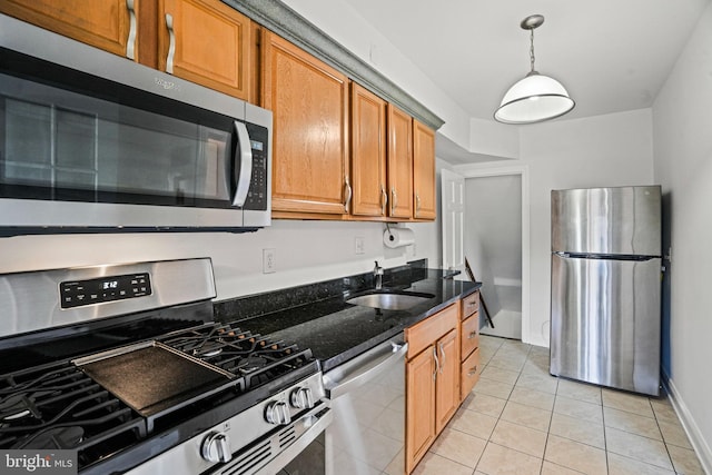 kitchen featuring dark stone counters, a sink, brown cabinetry, light tile patterned flooring, and appliances with stainless steel finishes