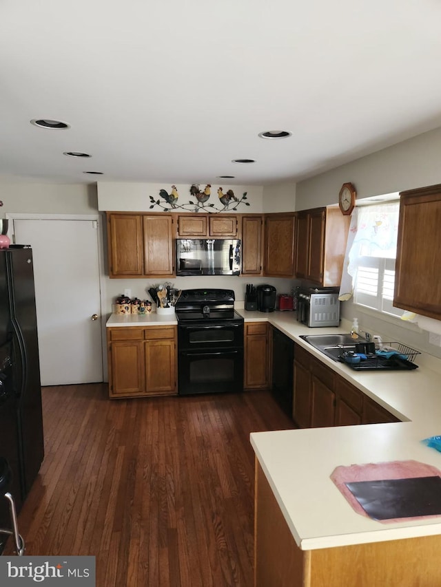 kitchen featuring light countertops, black appliances, brown cabinets, dark wood finished floors, and a sink
