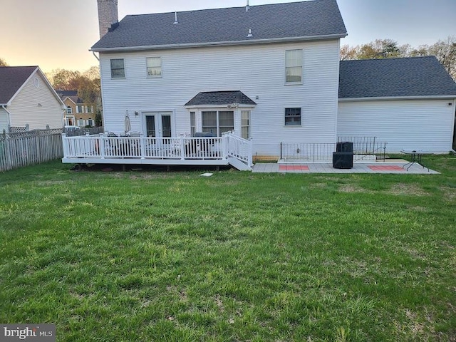 back of house with a chimney, a patio area, a wooden deck, fence, and a lawn