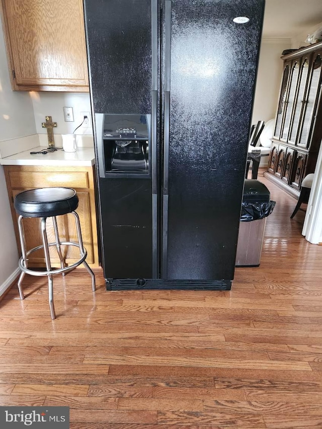 kitchen featuring black refrigerator with ice dispenser, light wood finished floors, light countertops, and ornamental molding