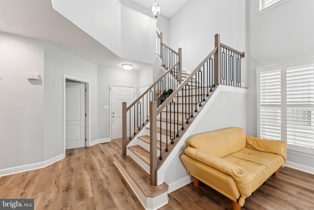 stairs with baseboards, wood finished floors, and a towering ceiling