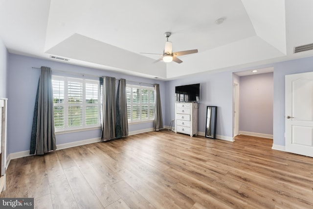 unfurnished bedroom with light wood-type flooring, baseboards, visible vents, and a tray ceiling