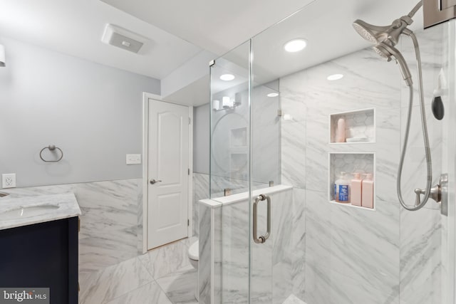 full bath with a wainscoted wall, a marble finish shower, tile walls, marble finish floor, and vanity
