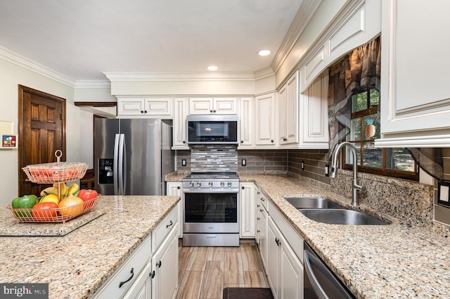 kitchen with crown molding, decorative backsplash, white cabinetry, a sink, and appliances with stainless steel finishes
