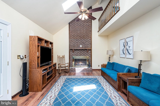 living area with wood finished floors, a fireplace, baseboards, ceiling fan, and high vaulted ceiling