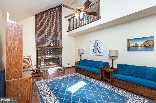 living area with a brick fireplace, beam ceiling, wood finished floors, high vaulted ceiling, and a ceiling fan