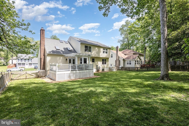 back of property with a fenced backyard, a wooden deck, a chimney, and a yard