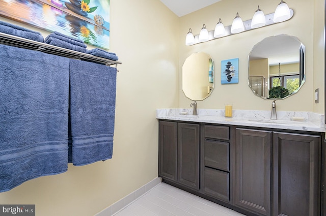 full bath featuring double vanity, tile patterned floors, a sink, and baseboards
