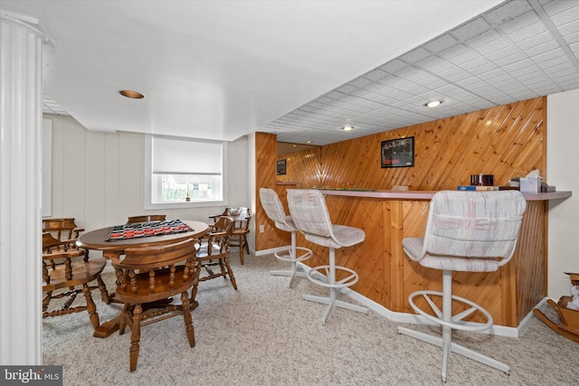 carpeted dining area with wooden walls and a bar