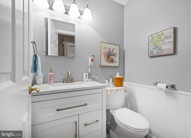 bathroom with a wainscoted wall, vanity, and toilet