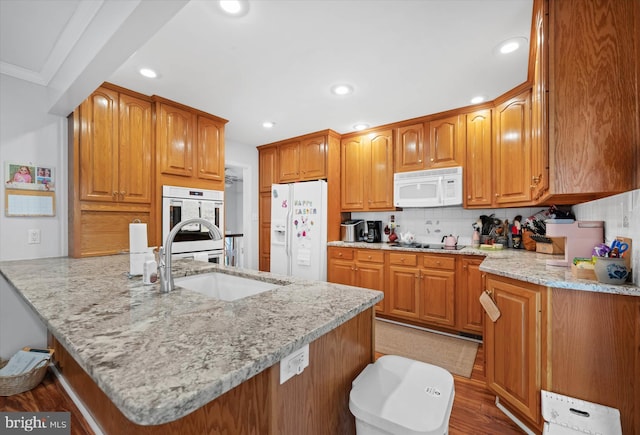 kitchen featuring a peninsula, a sink, backsplash, white appliances, and light stone countertops