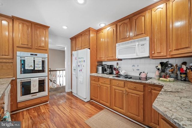 kitchen with decorative backsplash, brown cabinets, light wood-style floors, white appliances, and light stone countertops