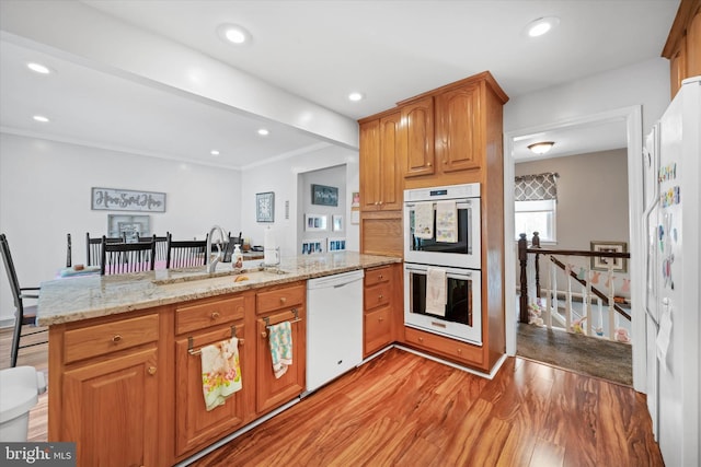 kitchen with a peninsula, light wood-style flooring, a sink, white appliances, and light stone countertops