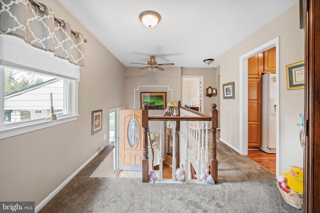 corridor with baseboards, an upstairs landing, and light colored carpet