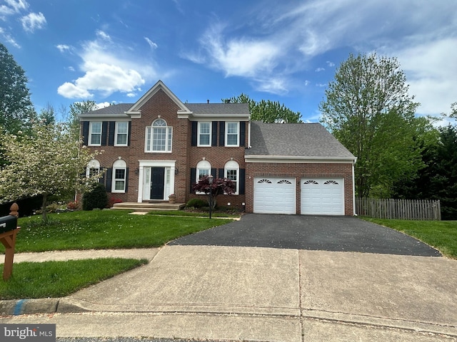 colonial-style house with a front lawn, a garage, aphalt driveway, brick siding, and fence