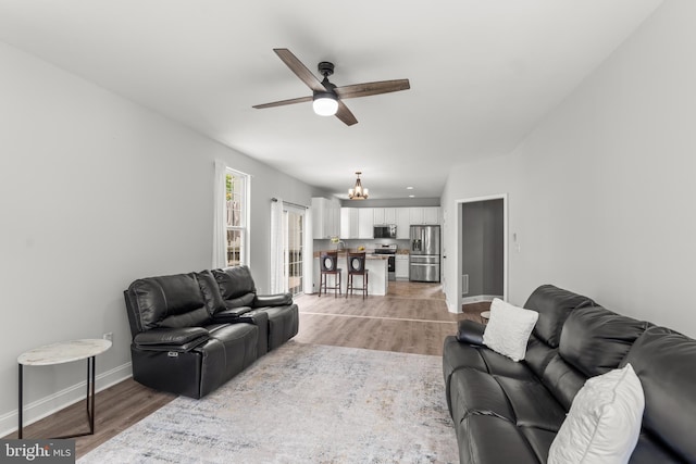 living area with light wood-style flooring, ceiling fan, and baseboards