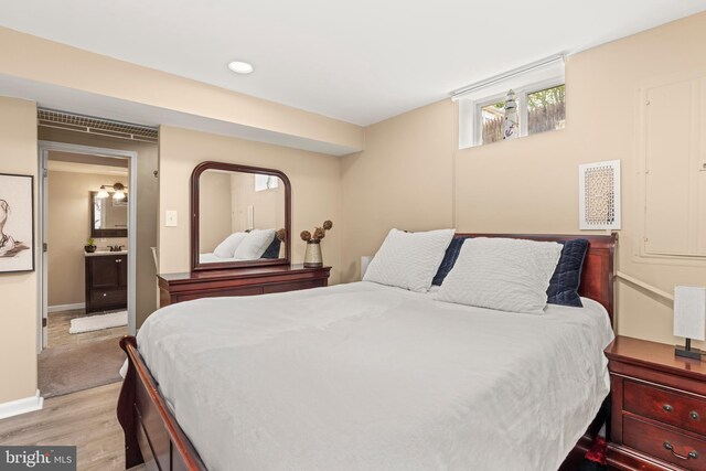 bedroom featuring light wood finished floors, baseboards, and ensuite bath