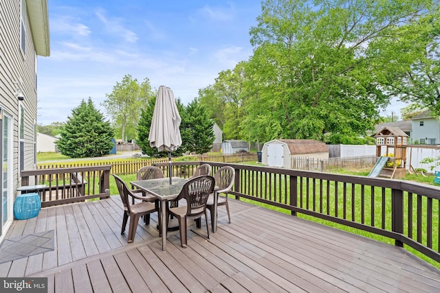 wooden terrace featuring a shed, outdoor dining area, an outdoor structure, and a playground