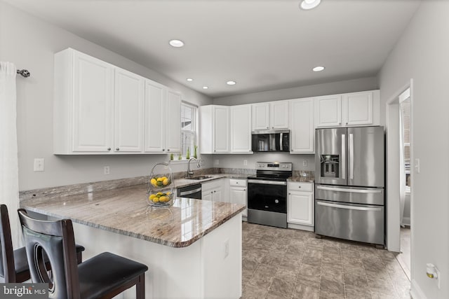 kitchen featuring stainless steel appliances, a sink, white cabinets, a peninsula, and light stone countertops