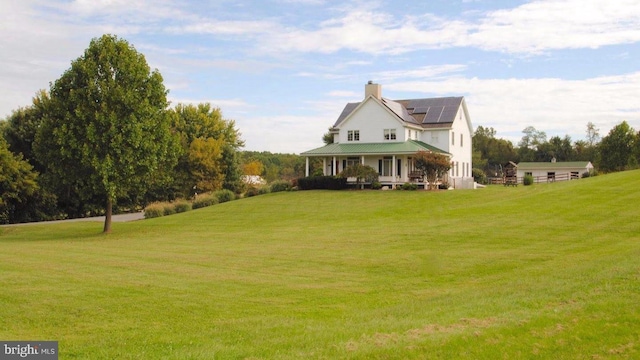 exterior space with a chimney, covered porch, a front yard, and solar panels