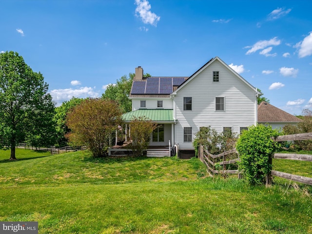 back of house with a yard, fence, a chimney, and solar panels