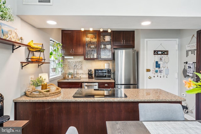 kitchen with dark brown cabinets, a sink, tasteful backsplash, glass insert cabinets, and appliances with stainless steel finishes