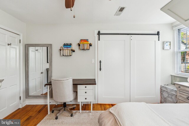 bedroom with wood finished floors, visible vents, and a barn door