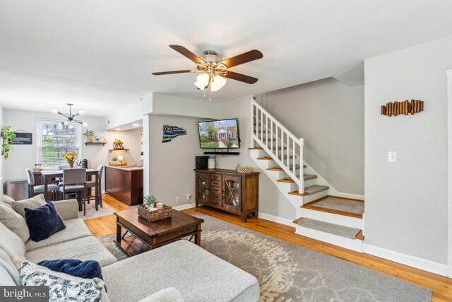 living room with ceiling fan with notable chandelier, baseboards, wood finished floors, and stairs
