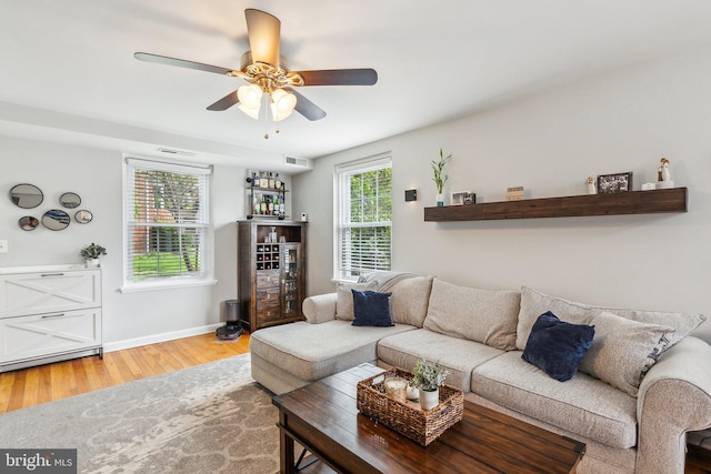 living area with wood finished floors, visible vents, a ceiling fan, a dry bar, and baseboards