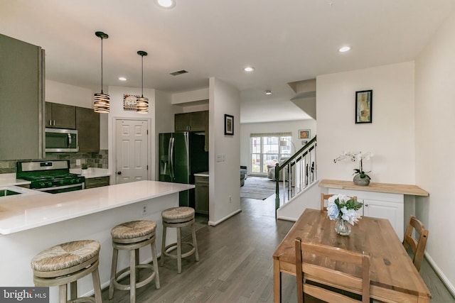 kitchen featuring light countertops, dark wood finished floors, a peninsula, appliances with stainless steel finishes, and recessed lighting